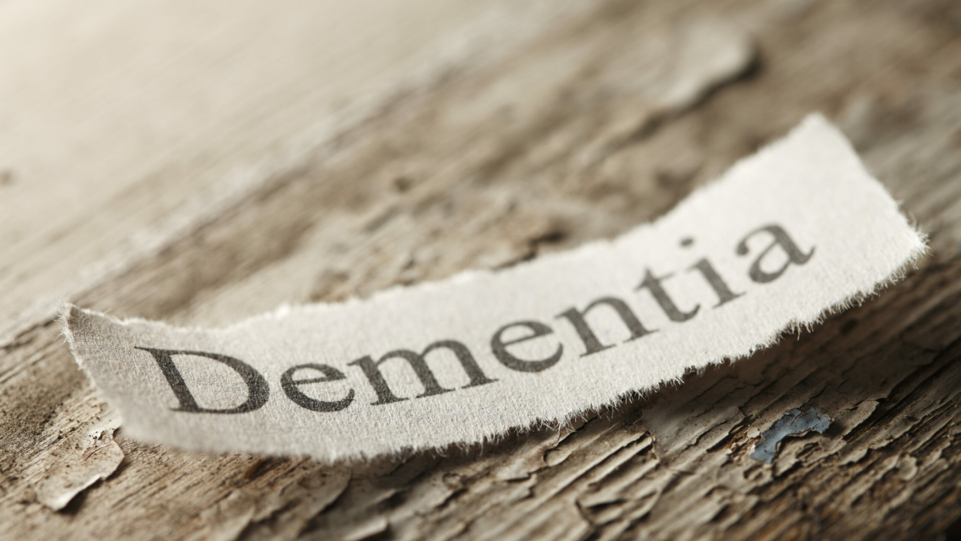 The word 'Dementia" on a torn piece of paper that rests on an old weathered piece of wood.  The old paint is flaking off of the wood surface to help convey the feeling of age.